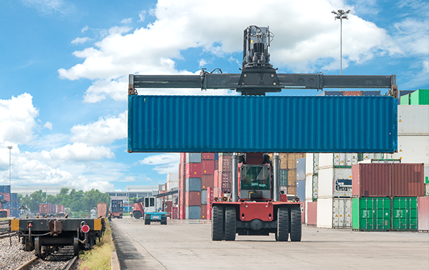 tractor moving blue shipping container onto a train car for shipping out