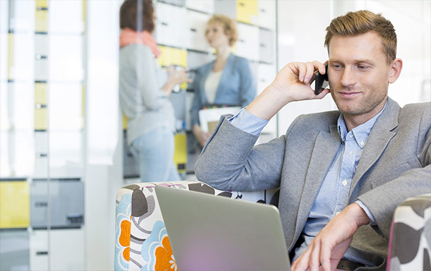 emo trans employee listening to a phone call involving supply chain solutions with coworkers in the back 