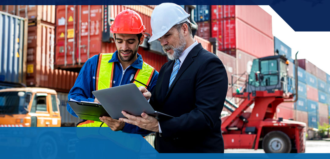Two men in hard hats look at tablets one i wearing a suit and the other a jumpsuit