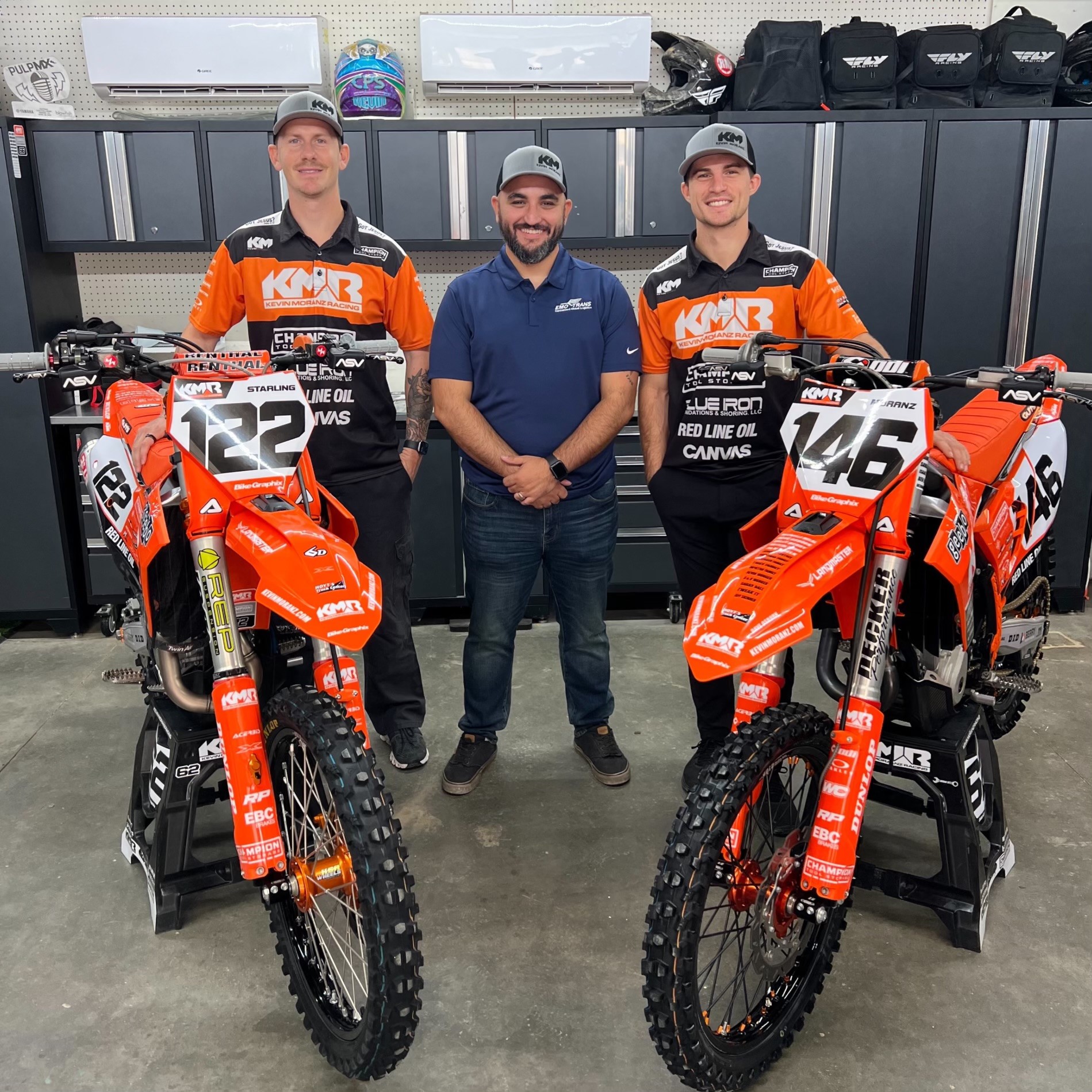 An EMO Trans employee stands with two dirt bike riders and their bikes