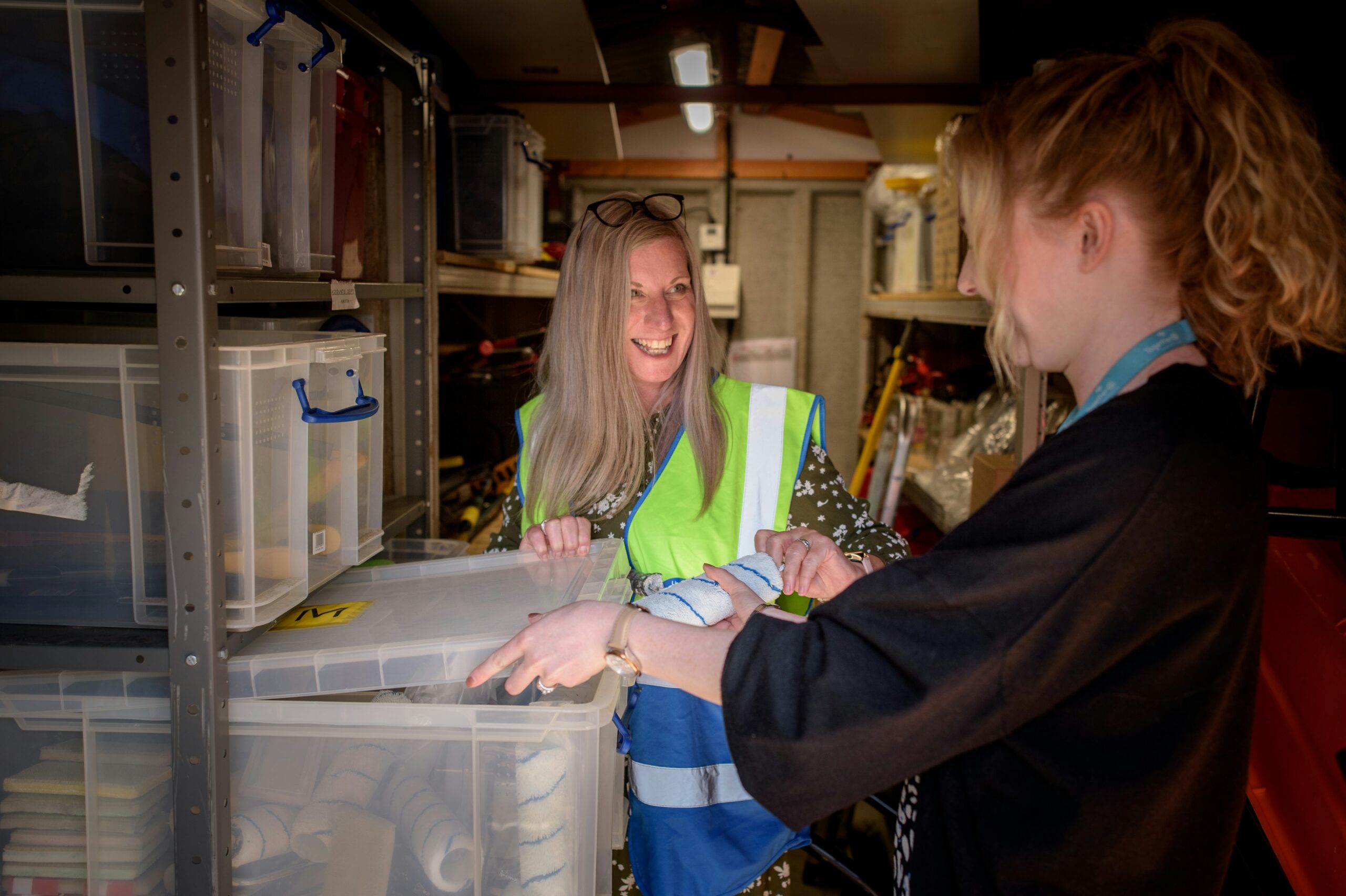 Two women in a fabric stock closet, one wears a safety vest